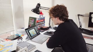 Young man sitting at a desk looking at a tablet computer with attached keyboard.