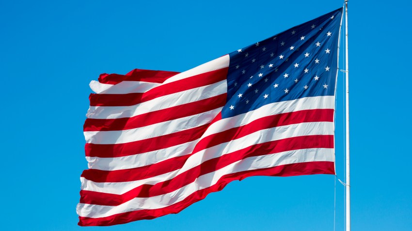 Stars and Stripes American flag blowing in the wind from flagpole on blue sky day in USA.