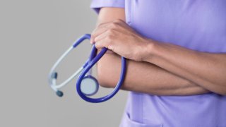 Female doctor holding stethoscope, arms folded.