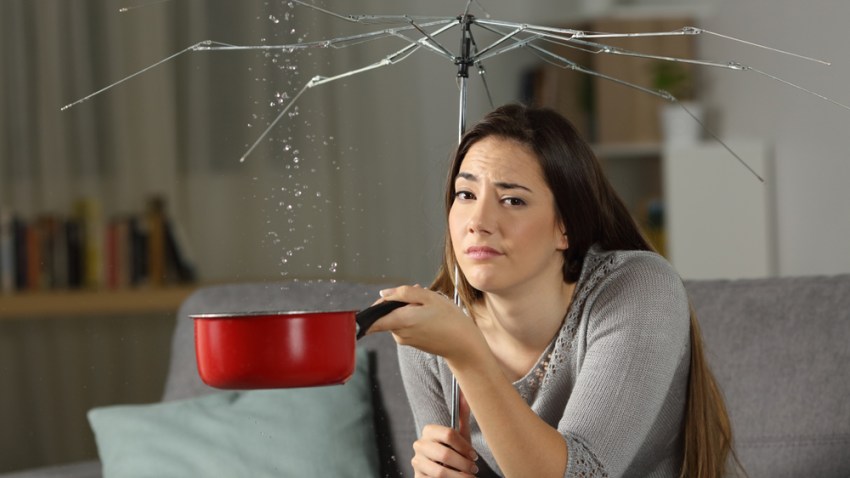 Foto de archivo de Shutterstock simula a una mujer con un paraguas roto y goteras en el techo.