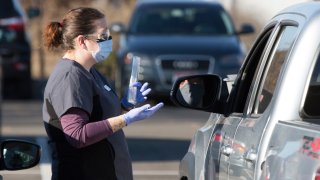 An employee gives instructions for self-administering a COVID-19 test in the parking lot at Primary Health Medical Group's clinic in Boise, Idaho, Tuesday, Nov. 24, 2020. The urgent-care clinic revamped into a facility for coronavirus patients as infections and deaths surge in Idaho and nationwide. Some 1,000 people have died due to COVID-19, and infections this week surpassed 100,000.
