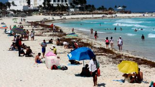 Turistas disfrutan las playas de Cancún aun cuando están con sargazo