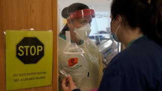 Clinical Nurse Supervisor Melinda Chapin, of Holderness, N.H., left, communicates through glass from inside a COVID-19 isolation room with registered nurse Rachel Chamberlin, of Cornish, N.H., right, at Dartmouth-Hitchcock Medical Center, in Lebanon, N.H., Monday, Jan. 3, 2022. Doctors and nurses, once lauded for their service, complain about burnout and a sense their neighbors are no longer treating the pandemic as a health emergency — despite day after day of record COVID-19 cases in the state.