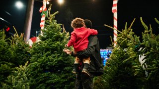 foto de archivo. Un padre carga a su hijo pequeño mientras compra el árbol de Navidad.