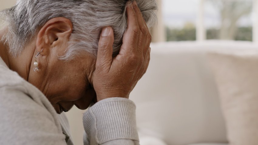 Mujer de edad avanzada se sujeta la cabeza con sus manos.