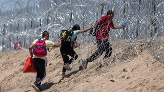 Inmigrantes intentan cruzar un alambre de púas para llegar a Estados Unidos.