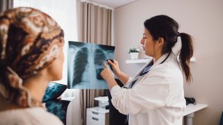 Mujer hispana experta dando consejos a un paciente con cáncer mientras examina una radiografía en la consulta del médico - foto de archivo.