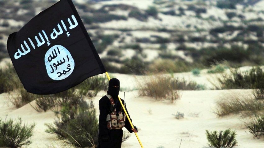 Islamic State/Iraq/Syria: A masked Islamic State soldier poses holding the ISIL banner somewhere in the deserts of Iraq or Syria. ISIL publicity image, 2015. (Photo by: Pictures from History/Universal Images Group via Getty Images)