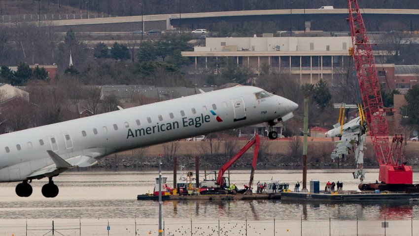 ARLINGTON, VIRGINIA – FEBRUARY 03: An airplane takes off as a large portion of the damaged plane fuselage is lifted from the Potomac River during recovery efforts after the American Airlines crash on February 03, 2025 in Arlington, Virginia. An American Airlines flight from Wichita, Kansas collided midair with a military Black Hawk helicopter while on approach to Ronald Reagan Washington National Airport on January 29, 2025 outside of Washington, DC. According to reports, there were no survivors among the 67 people onboard both aircraft. (Photo by Chip Somodevilla/Getty Images)